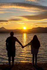 Young couple in love holding hands on a sandy beach near the sea at sunset spending romantic time on the weekend in summer. Sunrise by the sea bay