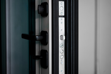 A slightly ajar thick armored door reveals a heavy lock mechanism and latch in a modern home entrance. Photo. Selective focusing. High resolution