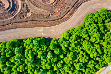 aerial drone view showing the stark contrast between a large open-pit mine and an adjacent lush green forest, highlighting the environmental impact of industry on nature