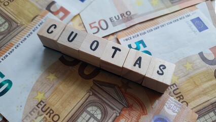 CUOTAS (INSTALLMENTS) word made of wooden letter cubes on pile of Euro banknotes.
