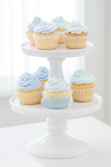 Light pastel-colored cupcakes with swirled frosting are displayed on a two-tiered white stand. Sweet indulgence, dessert presentation, minimal style