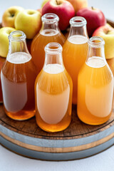 glass bottles filled with apple juice stand on a wooden barrel surrounded by fresh apples. Refreshing beverage selection, natural ingredients