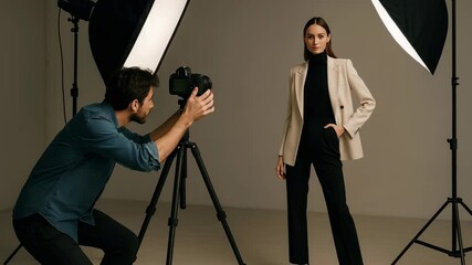 Professional video shoot in a studio with a mid-angle view. A photographer captures a model in stylish attire under soft lighting.