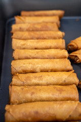 A tray full of golden-brown spring rolls neatly arranged for serving at a market or event