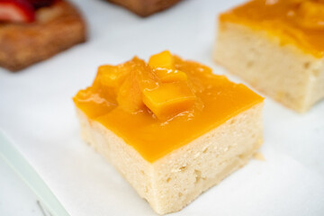 A yellow mango pastry with glossy top, neatly cut into a square and styled on a plate