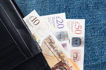 British banknotes in black leather wallet. Denim jeans pocket cash. Fifty pound notes partially...
