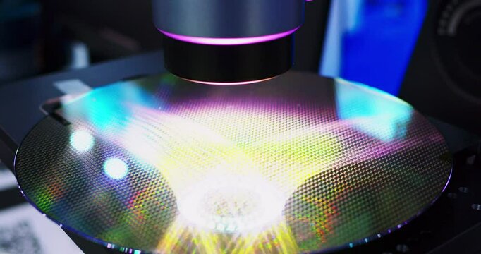 A silicon wafer with many electronic chips is illuminated by a flashlight. The camera moves, filming the silicon wafer. Close-up shot