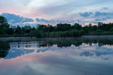 Peaceful lake with reeds and a colorful sunrise sky reflecting in calm water. Nature scene full of...
