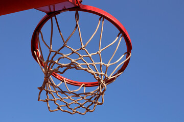 Basketball hoop, red ring and net, clear blue sky background, underview. Sunny day, outdoors sport court