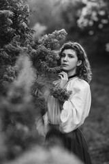 Young pretty caucasian woman in romantic outfit walking in blooming spring garden. Artistic outdoor photo of beautiful red-haired girl posing in fragrant lilac blossom.