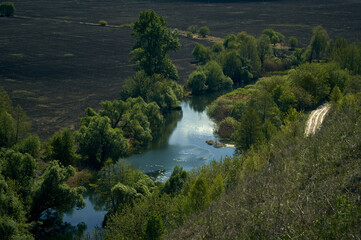 Spring, a freshly plowed field, trees and shrubs grow along the borders of the field, a small...