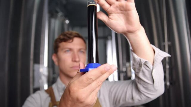 Brewer analyzing fresh dark beer sample for quality control in stainless steel tanks