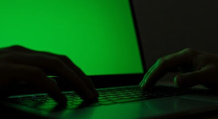 Hands typing on a laptop keyboard with a bright green screen, working.