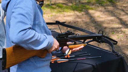 Teenager in blue hoodie loading black sport crossbow at shooting range in forest. Active...