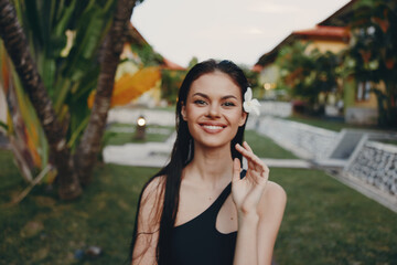 Smiling woman in black dress holding a flower standing in front of palm trees