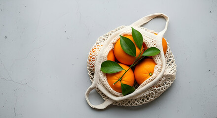 Fresh Oranges in a Natural Fiber Bag on a Gray Background with Green Leaves, Perfect for Health and Organic Lifestyle Themes