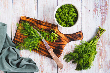 Chopped dill on a wooden board and a knife on the table top view