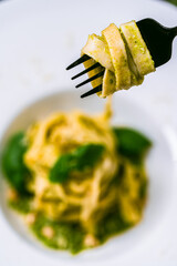 Fituccini al pesto on a white plate and a fork with spaghetti wound on a gray background. Vertical...
