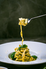 Fituccini al pesto on a white plate and a fork with spaghetti wound on a gray background. Vertical...