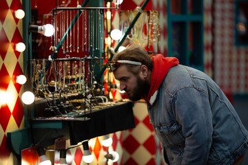 Horizontal street city photo. Young adult white man with beard, carnival deer antlers, blue denim...