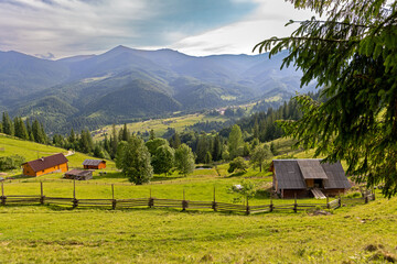 Scenic mountain valley with rural wooden houses. Wooden farm buildings and a rustic fence sit on a...