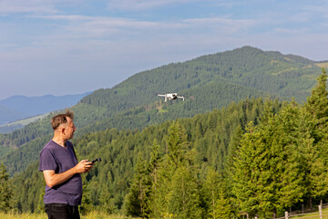 Man Flying Drone Over Mountain Forest Landscape. Person operating a drone with a remote controller...