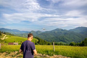 Man Operating Drone Over Scenic Mountain Landscape. Person flying a drone above lush green hills...