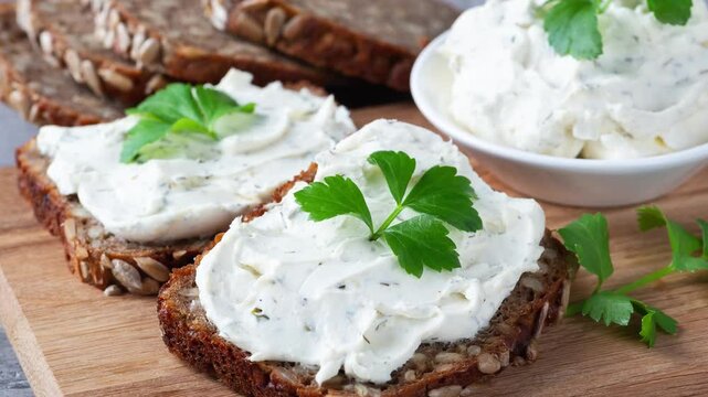 Home made bread on a wooden cutting board with curd cheese and ricotta and herbs. Decorated with green herbs
