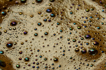 Texture of thick dark crema of black brewed coffee with colorful bubbles, view from the top