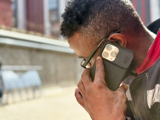 Happy African American man in a red jacket, talking on phone, blurred background. A black guy is talking on a smartphone blurred background and the concept of success, student with a phone. 