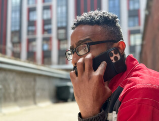 Happy African American man in a red jacket, talking on phone, blurred background. A black guy is talking on a smartphone blurred background and the concept of success, student with a phone. 