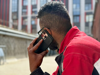 Happy African American man in a red jacket, talking on phone, blurred background. A black guy is talking on a smartphone blurred background and the concept of success, student with a phone. 