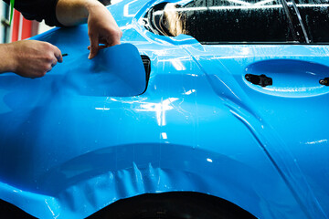 Detailing technician trims blue PPF on a car panel for perfect contour fit. Cutting blue PPF with...