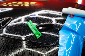 PPF Paint Protection Film Tools on Car Hood. Car wrap tools, including squeegees and magnets on wet...