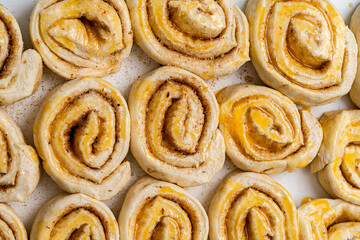 Making homemade cinnamon puff pastry buns. Raw dough rolls greased with egg yolk.