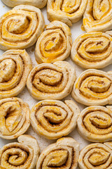 Making homemade cinnamon puff pastry buns. Raw dough rolls greased with egg yolk.