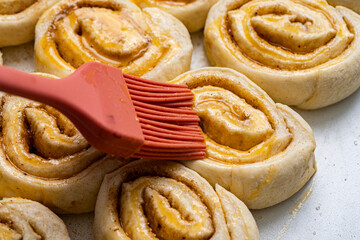 Making homemade cinnamon puff text buns. The brush greases raw dough rolls with egg yolk.