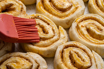 Making homemade cinnamon puff text buns. The brush greases raw dough rolls with egg yolk.