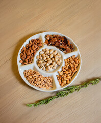 Assorted nuts on white ceramic plate over wooden background – almonds, pistachios, peanuts, pecans and cashews