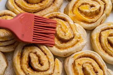 Making homemade cinnamon puff text buns. The brush greases raw dough rolls with egg yolk.