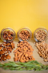 Pecans almonds and peanuts spilling from glass jars on wooden surface with yellow background