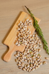 Pistachio nuts spilling from wooden cutting board with sprig of rosemary on light wood background