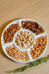 Selection of assorted nuts including pistachios almonds cashews peanuts and pecans in ceramic tray...