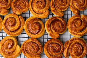 Delicious homemade cinnamon puff pastry buns in the shape of a roll or snail on a black grill. Close-up. View from above.