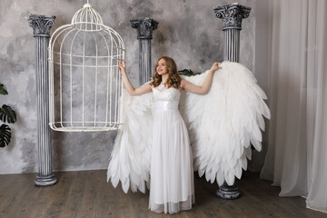 Beautiful girl with white angel wings near white cage