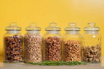 Glass jars with pecans peanuts almonds cashews and walnuts on wooden surface with yellow background...