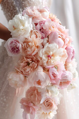 Fototapeta premium Lush bridal bouquet of pastel pink, peach, and ivory peonies held by a bride in a sequin wedding dress