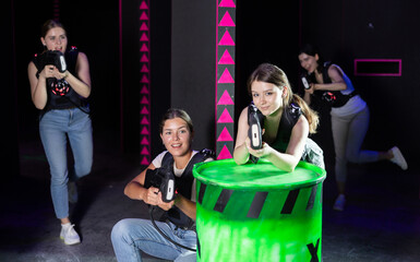 Laser tag players cheerful positive smiling girls playing in teams in dark laser tag room