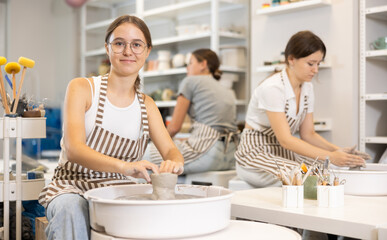 Young woman teacher and two girl students sculpt ceramic products on pottery wheel