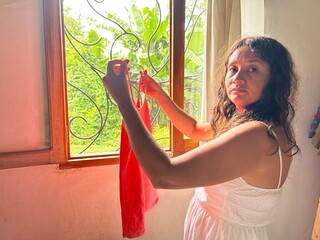 stressed and serious woman looks at the camera, while holding a red T-shirt in her hand, she is...